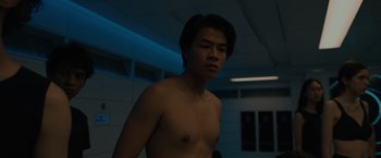 Movie still from “Voyagers” (2021), directed by Neil Burger – A man with no shirt standing in a room; Medium shot, Low angle