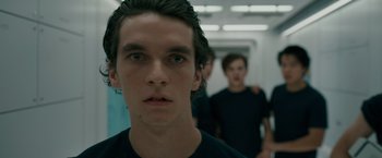 Movie still from “Voyagers” (2021), directed by Neil Burger – A young man in a black t - shirt is in a hallway; Close Up shot, Low angle