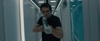 Movie still from “Voyagers” (2021), directed by Neil Burger – A man in a black t - shirt holding a gun in a hallway; Close Up shot, Low angle