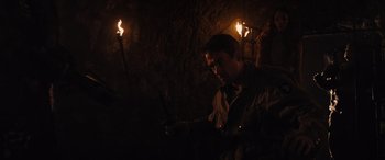Movie still from “WarHunt” (2022), directed by Mauro Borrelli – A man holding two torches in a dark forest; Medium shot, Over the shoulder angle