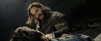 Movie still from “Warcraft” (2016), directed by Duncan Jones – A man with long hair and a beard sitting in front of a bed; Medium shot, Over the shoulder angle