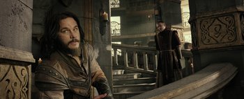 Movie still from “Warcraft” (2016), directed by Duncan Jones – A man with long hair and a beard standing in front of a staircase; Medium shot, Over the shoulder angle