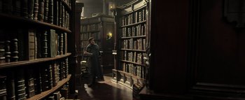 Movie still from “Warcraft” (2016), directed by Duncan Jones – A man standing in front of a bookcase in a room; Wide shot, High angle