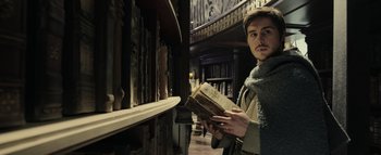 Movie still from “Warcraft” (2016), directed by Duncan Jones – A man is holding an old book in a library; Medium shot, Low angle