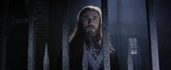 Movie still from “Warcraft” (2016), directed by Duncan Jones – A man with long hair and a beard standing behind a metal fence; Close Up shot, Low angle