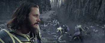 Movie still from “Warcraft” (2016), directed by Duncan Jones – A man with a beard is standing in front of a group of people; Close Up shot, Over the shoulder angle