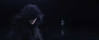 A woman in a black robe standing next to a body of water at night