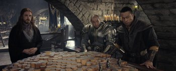 Movie still from “Warcraft” (2016), directed by Duncan Jones – A man in a suit of armor is sitting at a table; Medium shot, High angle