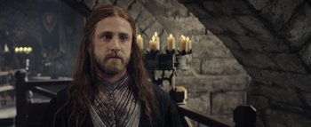 Movie still from “Warcraft” (2016), directed by Duncan Jones – A man with long hair and a beard standing in front of candles; Close Up shot, Over the shoulder angle