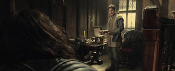 Movie still from “Warcraft” (2016), directed by Duncan Jones – A man standing next to a wooden table; Medium shot, Over the shoulder angle