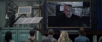 Movie still from “Warm Bodies” (2013), directed by Jonathan Levine – People are standing in front of a large television screen; Medium shot, Over the shoulder angle