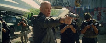 Movie still from “Warm Bodies” (2013), directed by Jonathan Levine – An older bald man holding a gun in his hand; Medium shot, Over the shoulder angle