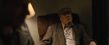 Movie still from “Warrior” (2011), directed by Gavin O'Connor – An older man wearing a suit and a hat is sitting in a chair; Medium shot, Over the shoulder angle