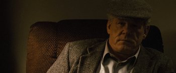 Movie still from “Warrior” (2011), directed by Gavin O'Connor – An older man wearing a suit and a hat sitting on a couch; Close Up shot, Low angle
