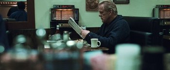 Movie still from “Warrior” (2011), directed by Gavin O'Connor – An older man sitting at a table reading a newspaper; Medium shot, Over the shoulder angle