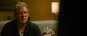 Movie still from “Warrior” (2011), directed by Gavin O'Connor – A man sitting on top of a couch in a living room; Close Up shot, Over the shoulder angle