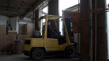 Movie still from “Fargo” (2014), created by Noah Hawley – A man driving a yellow forklift in a warehouse; Wide shot, Low angle