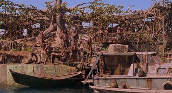 Movie still from “Waterworld” (1995), directed by Kevin Reynolds – A group of people standing on top of a boat next to trees; Extreme Wide shot, High angle
