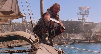 Movie still from “Waterworld” (1995), directed by Kevin Reynolds – A man standing on top of a boat holding a knife; Medium shot, Low angle