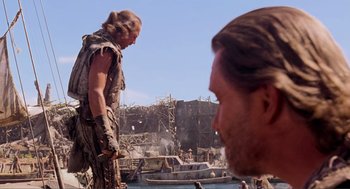 Movie still from “Waterworld” (1995), directed by Kevin Reynolds – A man standing next to another man on a beach; Medium shot, Over the shoulder angle