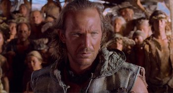 Movie still from “Waterworld” (1995), directed by Kevin Reynolds – A person with a bunch of people in the background; Close Up shot, Over the shoulder angle