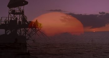 Movie still from “Waterworld” (1995), directed by Kevin Reynolds – A person standing on top of a tower next to a body of water at sunset; Extreme Wide shot, Low angle