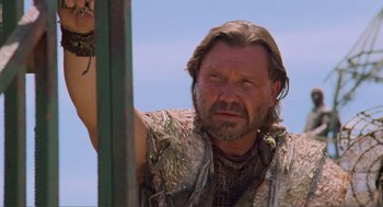 Movie still from “Waterworld” (1995), directed by Kevin Reynolds – A man with long hair and a beard is looking at the camera; Close Up shot, Low angle