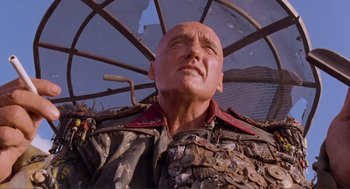 Movie still from “Waterworld” (1995), directed by Kevin Reynolds – A man with a bald head is under an umbrella; Close Up shot, Low angle