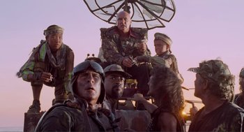 Movie still from “Waterworld” (1995), directed by Kevin Reynolds – A group of people standing around a man with an umbrella; Medium shot, Low angle