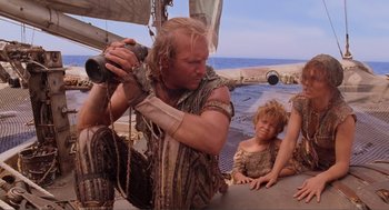 Movie still from “Waterworld” (1995), directed by Kevin Reynolds – A man with a beard is looking through a telescope on a boat; Medium shot, Low angle