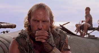 Movie still from “Waterworld” (1995), directed by Kevin Reynolds – A person on a boat with his hand to his mouth; Close Up shot, Over the shoulder angle