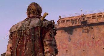 Movie still from “Waterworld” (1995), directed by Kevin Reynolds – A man in a leather jacket holding a sword in front of a building; Wide shot, Low angle