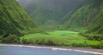 Movie still from “Waterworld” (1995), directed by Kevin Reynolds – A view of a lush green valley and a body of water in the distance; Extreme Wide shot, High angle