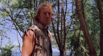 Movie still from “Waterworld” (1995), directed by Kevin Reynolds – A man in a vest standing next to a tree; Close Up shot, Low angle