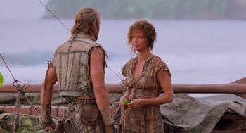 Movie still from “Waterworld” (1995), directed by Kevin Reynolds – A woman standing next to a man holding a green apple; Medium shot, Over the shoulder angle