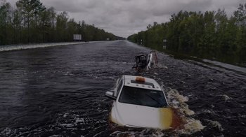 Movie still from “We Feed People” (2022), directed by Ron Howard – A white car in the middle of a flooded road; Extreme Wide shot, High angle