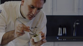 Movie still from “We Feed People” (2022), directed by Ron Howard – A man in a chef's outfit holding a knife and a spoon in a bowl of food; Close Up shot, Low angle