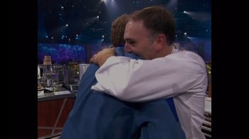 Movie still from “We Feed People” (2022), directed by Ron Howard – Two people hugging each other on a television set; Medium shot, Over the shoulder angle