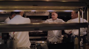 Movie still from “We Feed People” (2022), directed by Ron Howard – A man standing in front of two other men in front of an oven in a kitchen; Medium shot, Low angle