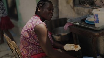Movie still from “We Feed People” (2022), directed by Ron Howard – A woman sitting in front of an oven holding a piece of food; Close Up shot, High angle