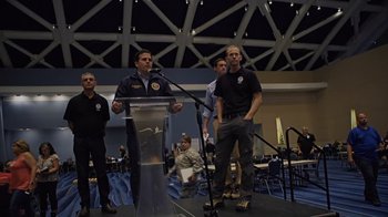 Movie still from “We Feed People” (2022), directed by Ron Howard – A man standing at a podium in front of a microphone; Wide shot, Low angle