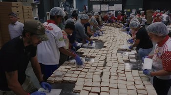 Movie still from “We Feed People” (2022), directed by Ron Howard – A group of people making sandwiches on a table; Wide shot, Overhead angle