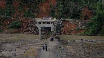 Movie still from “We Feed People” (2022), directed by Ron Howard – A group of people standing next to a bridge that has been washed out; Extreme Wide shot, High angle