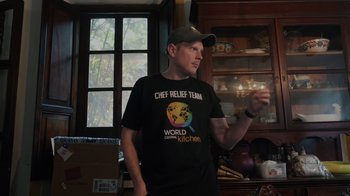 Movie still from “We Feed People” (2022), directed by Ron Howard – A man wearing a chef relief team t - shirt in a kitchen; Close Up shot, Over the shoulder angle