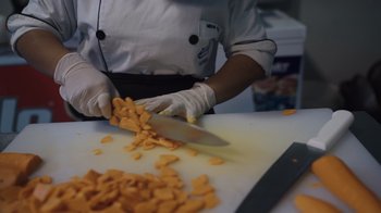 Movie still from “We Feed People” (2022), directed by Ron Howard – A person in a kitchen slicing cheese on a cutting board; Extreme Close Up shot, Low angle