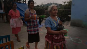Movie still from “We Feed People” (2022), directed by Ron Howard – Two older women standing next to each other holding items; Medium shot, High angle