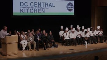 Movie still from “We Feed People” (2022), directed by Ron Howard – A group of people sitting on a stage wearing chef's hats; Wide shot, High angle