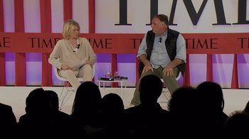 Movie still from “We Feed People” (2022), directed by Ron Howard – A man and a woman sitting on chairs in front of an audience; Medium shot, Low angle