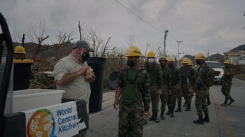 Movie still from “We Feed People” (2022), directed by Ron Howard – A group of people in military uniforms are standing in a line; Medium shot, Over the shoulder angle