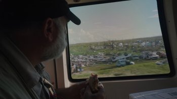 Movie still from “We Feed People” (2022), directed by Ron Howard – A man sitting in a vehicle with a sandwich in front of him; Medium shot, Over the shoulder angle
